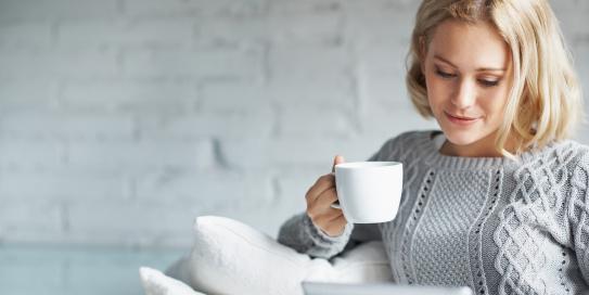 Frau schaut entspannt auf ihr Tablett und trinkt Kaffee