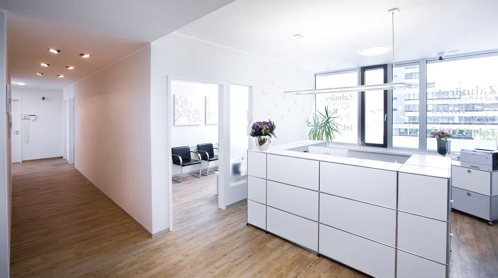 Moderner Empfangsbereich einer Zahnarztpraxis mit großem Tresen, hellem Holzboden und Blick in das Wartezimmer.